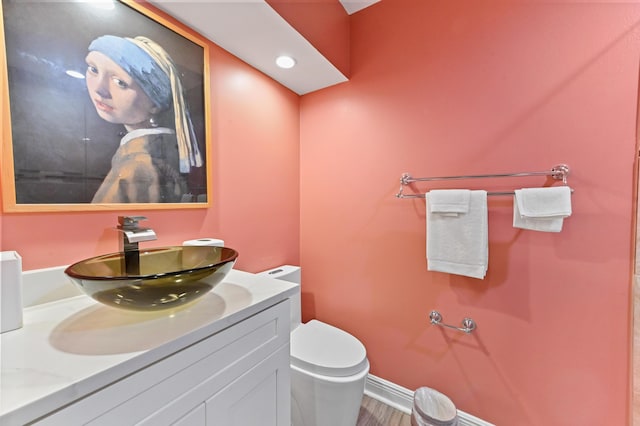 bathroom with toilet, baseboards, wood finished floors, and vanity