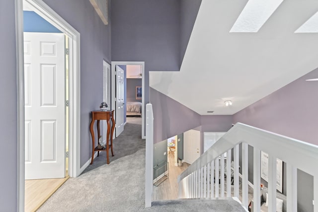 stairway with a skylight, baseboards, wood finished floors, carpet, and high vaulted ceiling