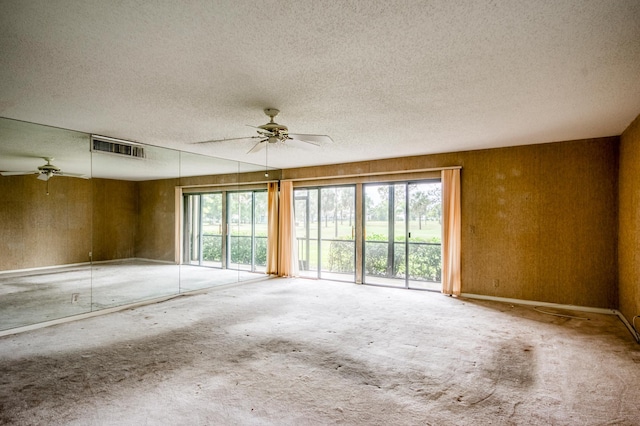 empty room with ceiling fan, a textured ceiling, and wooden walls