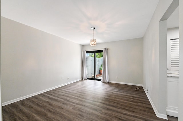 spare room featuring dark wood-type flooring and a notable chandelier