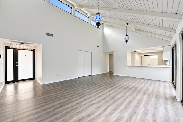 unfurnished living room featuring light hardwood / wood-style flooring, beam ceiling, and a towering ceiling