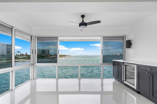 unfurnished sunroom with ceiling fan, a water view, and beverage cooler