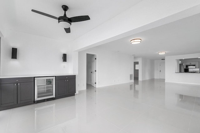 unfurnished living room with ceiling fan, light tile patterned floors, wine cooler, and bar area