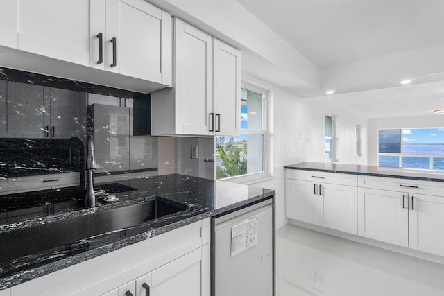 kitchen with tasteful backsplash, sink, white cabinetry, dishwashing machine, and dark stone counters