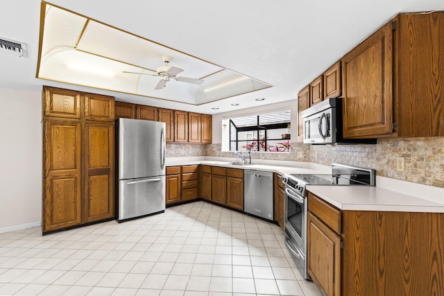 kitchen with a raised ceiling, stainless steel appliances, ceiling fan, sink, and backsplash