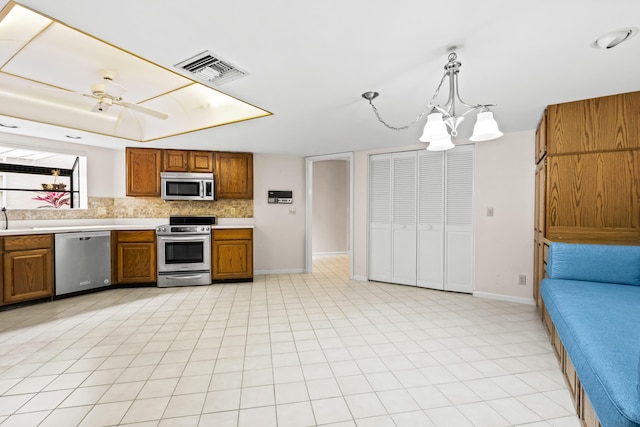 kitchen featuring a raised ceiling, appliances with stainless steel finishes, hanging light fixtures, ceiling fan with notable chandelier, and tasteful backsplash