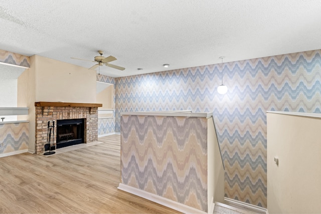 unfurnished living room featuring a textured ceiling, ceiling fan, light hardwood / wood-style flooring, and a fireplace