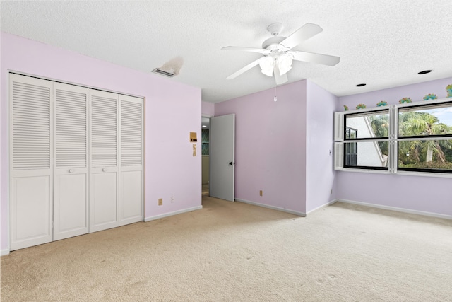 unfurnished bedroom featuring ceiling fan, a closet, light carpet, and a textured ceiling