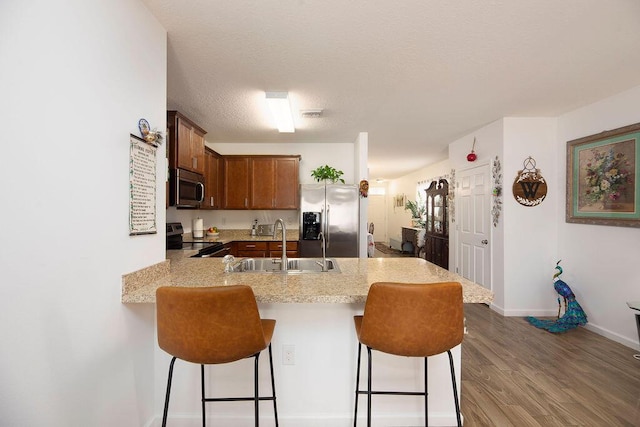 kitchen with a kitchen bar, stainless steel appliances, sink, kitchen peninsula, and hardwood / wood-style flooring