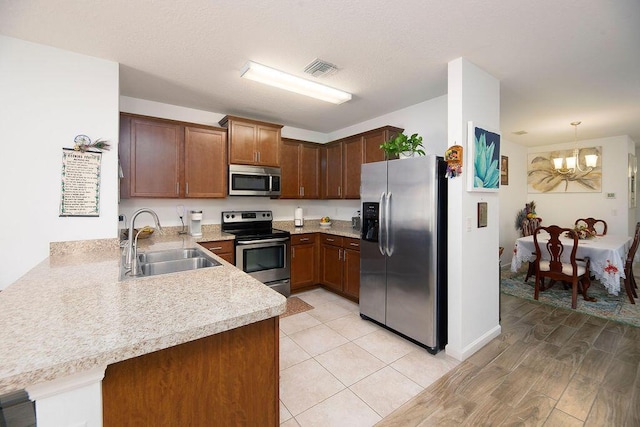 kitchen with appliances with stainless steel finishes, a chandelier, kitchen peninsula, and sink