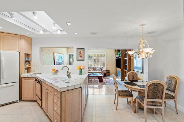 kitchen with kitchen peninsula, light brown cabinets, hanging light fixtures, white refrigerator, and sink