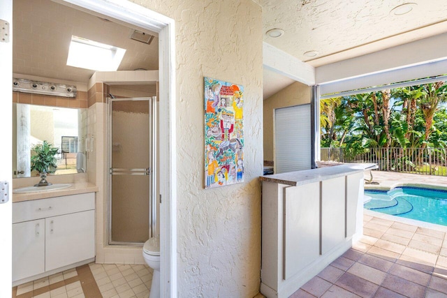 bathroom with vanity, toilet, vaulted ceiling with skylight, and a shower with door