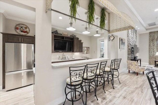 kitchen with a kitchen bar, stainless steel fridge, sink, and dark brown cabinetry