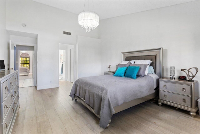 bedroom with an inviting chandelier, a towering ceiling, and light hardwood / wood-style floors