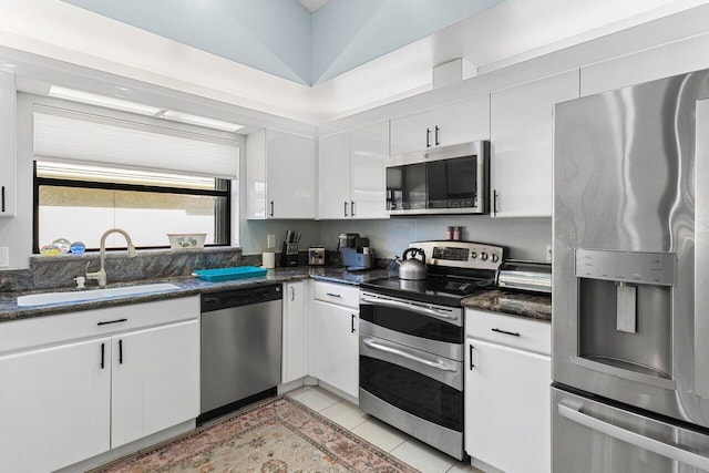 kitchen featuring sink, white cabinetry, dark stone counters, light tile patterned floors, and stainless steel appliances