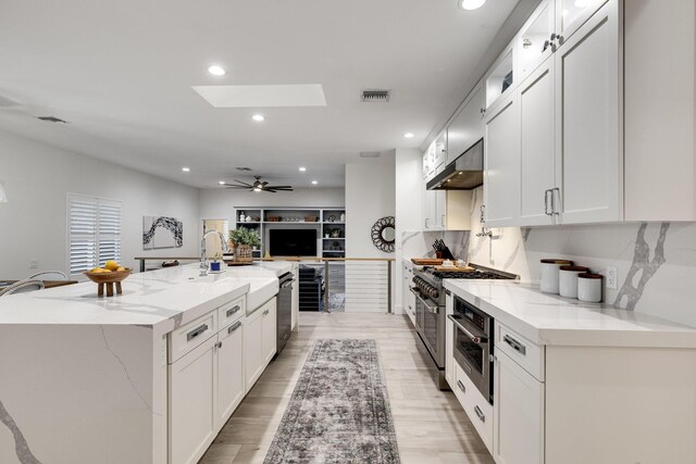 kitchen with white cabinetry, light stone countertops, a large island, and a skylight