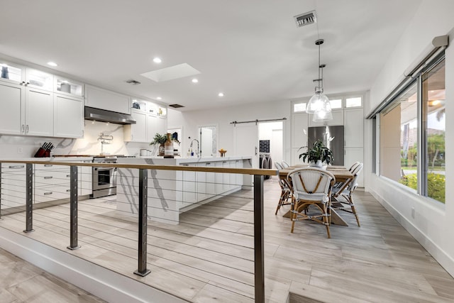 kitchen with appliances with stainless steel finishes, a skylight, ventilation hood, white cabinetry, and hanging light fixtures