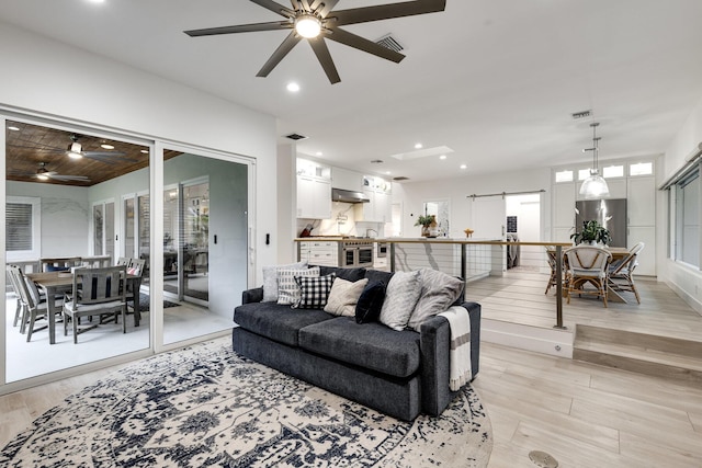 living room with light hardwood / wood-style floors, a barn door, and ceiling fan