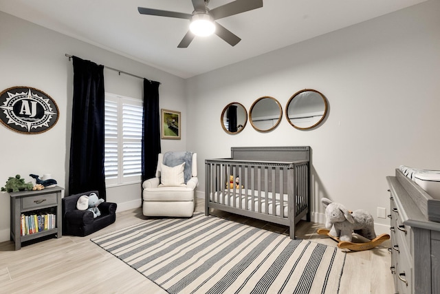 bedroom featuring a crib, light hardwood / wood-style floors, and ceiling fan