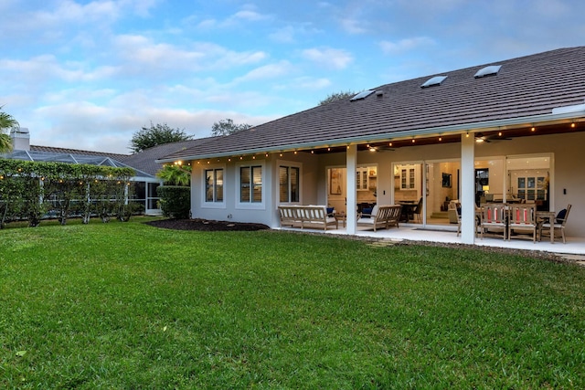 back of property featuring ceiling fan, a patio, glass enclosure, and a lawn