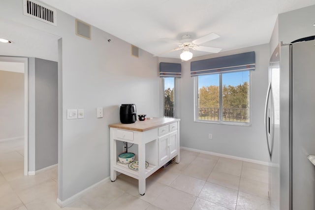 kitchen with light tile patterned floors, wooden counters, stainless steel refrigerator, white cabinets, and ceiling fan