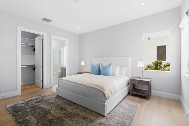 bedroom with ensuite bath, a walk in closet, a closet, and light hardwood / wood-style flooring