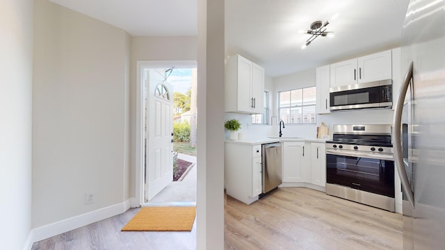 kitchen with light hardwood / wood-style floors, white cabinets, appliances with stainless steel finishes, and sink