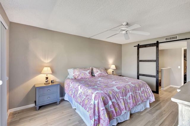 bedroom with light hardwood / wood-style floors, a barn door, and a textured ceiling