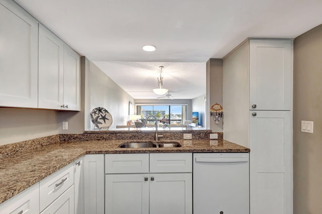 kitchen featuring dark stone countertops, dishwasher, sink, and white cabinets