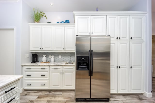 kitchen with stainless steel refrigerator with ice dispenser, light stone counters, white cabinets, and tasteful backsplash