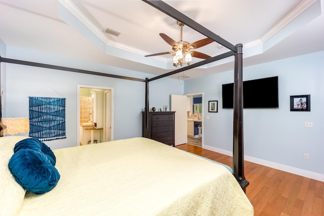 bedroom featuring ensuite bathroom, ceiling fan, a tray ceiling, wood-type flooring, and crown molding