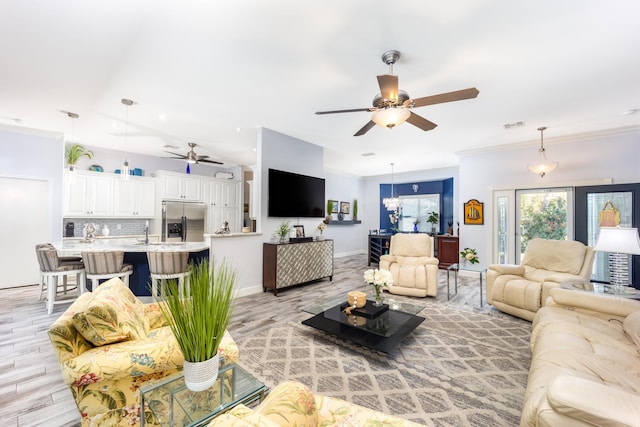 living room with crown molding, ceiling fan with notable chandelier, and light hardwood / wood-style floors