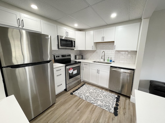 kitchen with a drop ceiling, appliances with stainless steel finishes, sink, and white cabinetry