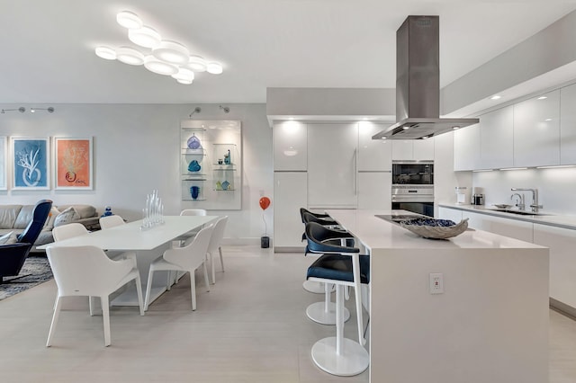 kitchen featuring island exhaust hood, double oven, a breakfast bar, a kitchen island, and white cabinetry