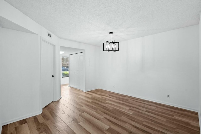 unfurnished dining area featuring hardwood / wood-style flooring, an inviting chandelier, and a textured ceiling