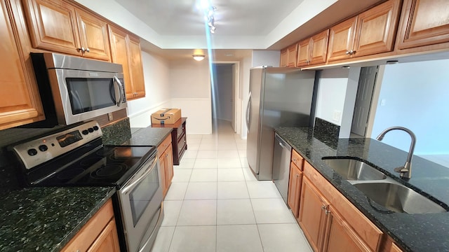 kitchen featuring appliances with stainless steel finishes, dark stone countertops, sink, and light tile patterned floors