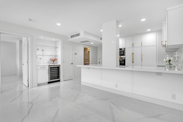 kitchen featuring double oven, white cabinets, kitchen peninsula, and beverage cooler