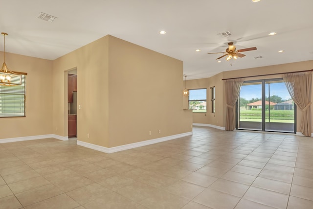 tiled spare room with ceiling fan with notable chandelier