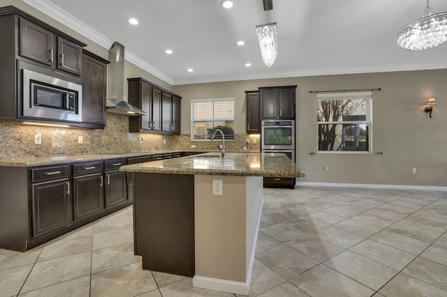 kitchen with wall chimney range hood, appliances with stainless steel finishes, a kitchen island with sink, hanging light fixtures, and ornamental molding