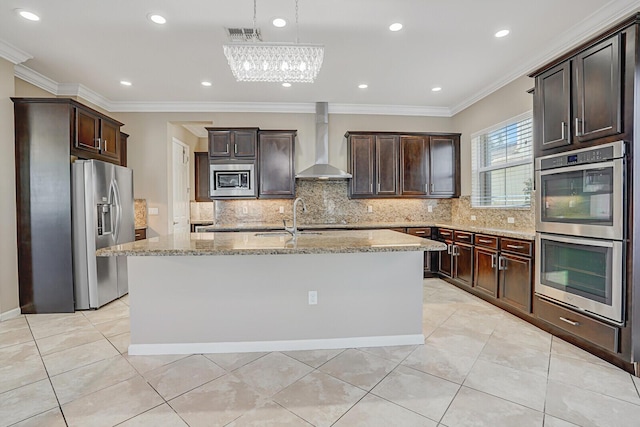 kitchen with stainless steel appliances, light stone countertops, ornamental molding, an island with sink, and wall chimney exhaust hood