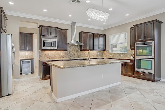 kitchen featuring appliances with stainless steel finishes, wine cooler, ornamental molding, a center island with sink, and wall chimney exhaust hood