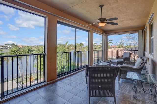 sunroom with ceiling fan and a water view