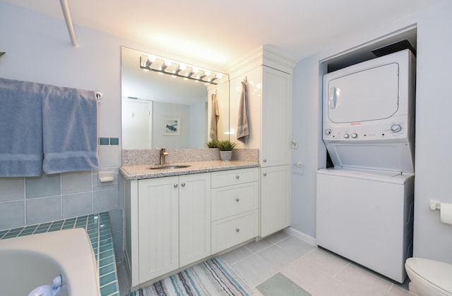 bathroom featuring toilet, a bathtub, tile patterned floors, stacked washer and clothes dryer, and vanity