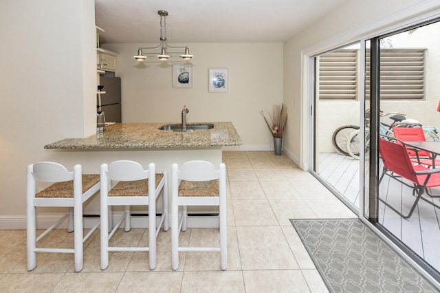 kitchen featuring sink, fridge, decorative light fixtures, light stone counters, and kitchen peninsula