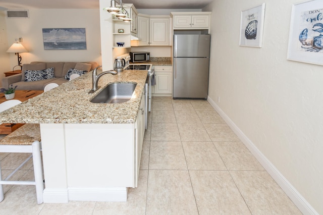 kitchen with light stone counters, hanging light fixtures, a breakfast bar, appliances with stainless steel finishes, and sink