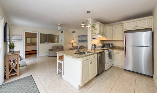 kitchen with kitchen peninsula, stainless steel appliances, cream cabinetry, and light stone countertops