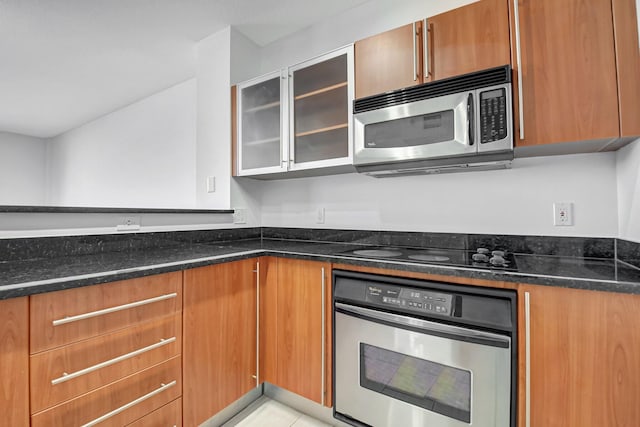 kitchen featuring light tile patterned floors, appliances with stainless steel finishes, and dark stone counters