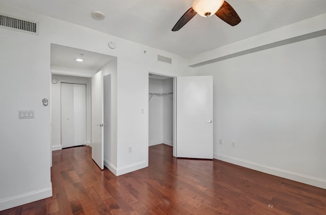 unfurnished bedroom featuring ceiling fan, a spacious closet, a closet, and dark hardwood / wood-style floors