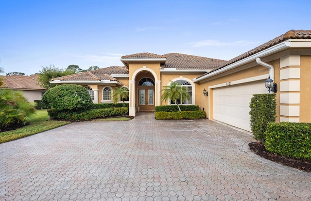 view of front of house featuring stucco siding, a tile roof, decorative driveway, french doors, and an attached garage