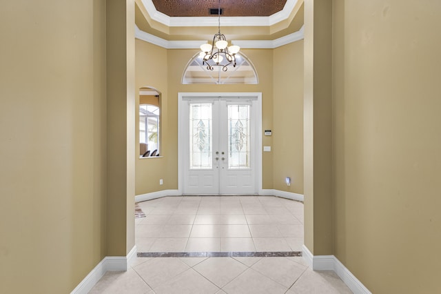 tiled entryway featuring french doors, a raised ceiling, ornamental molding, and a chandelier